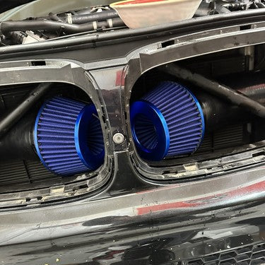 Two bright blue anodized cone air filters installed side-by-side in the front intake openings of a black car.