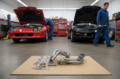 Red Camaro and black Firebird in a workshop with the stainless headers kit on the floor