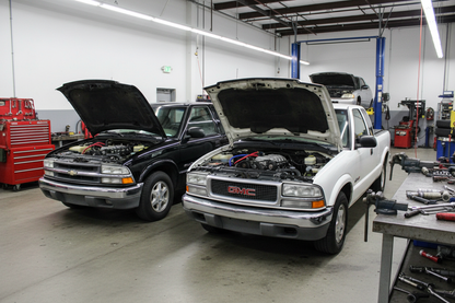 Chevrolet S10 Pickup and GMC Sonoma 1999 Pickup both parked in a mechanic shop with the hoods popped open